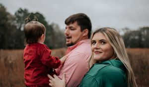 Family portrait in an autumn field with natural woods in the background.