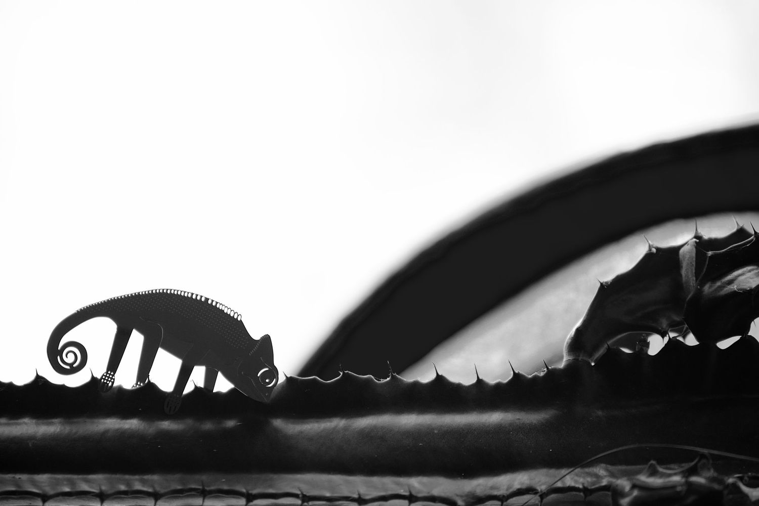 A decorative metal chameleon appears to be walking along a cactus landscape.