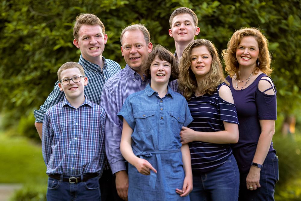 Outdoor family portrait of group in coordinated blue outfits against green foliage.