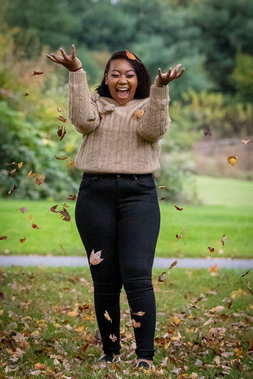 Person in beige sweater joyfully tossing autumn leaves in the air.