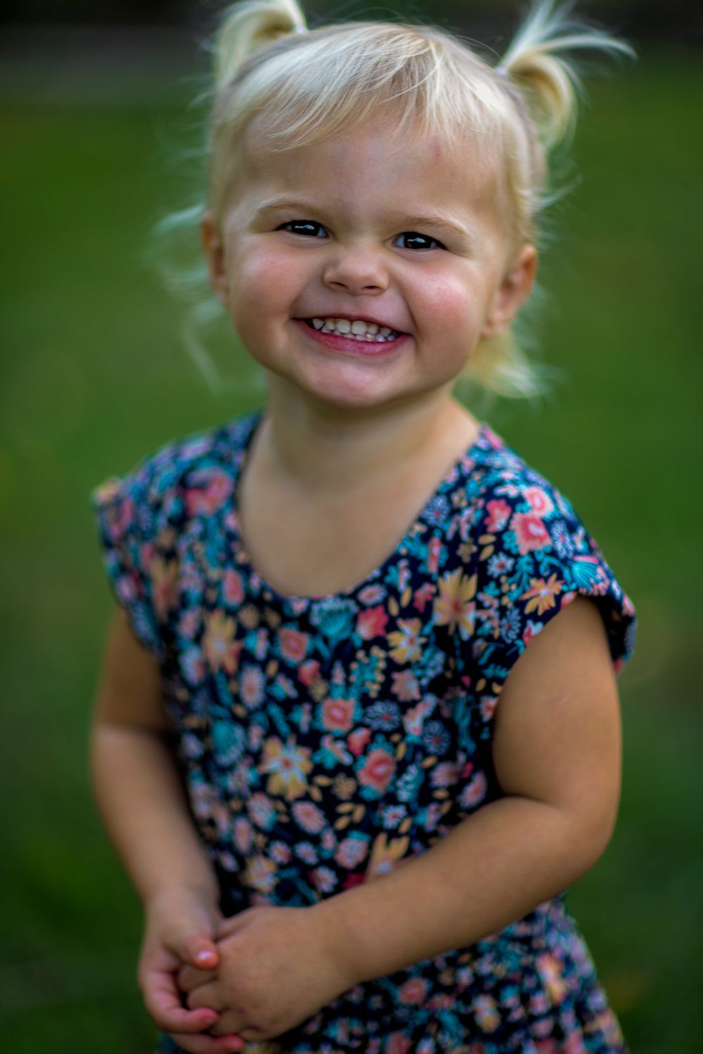 Child in floral dress with pigtails smiling brightly outdoors.