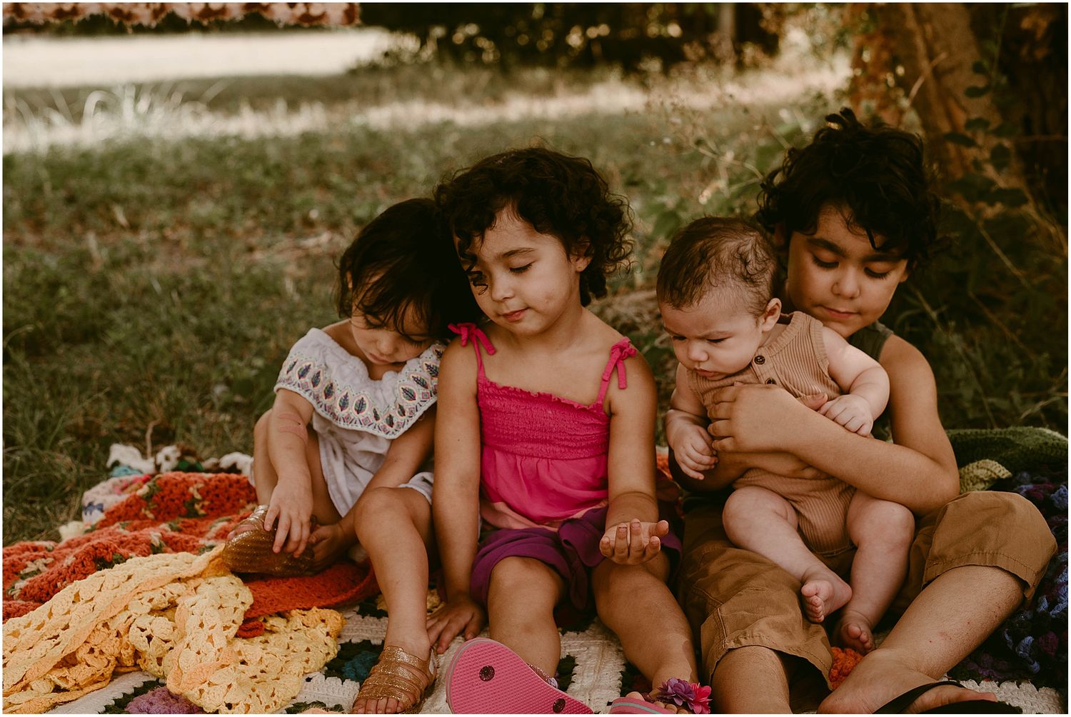 Children sitting together on a colorful blanket outdoors during a sunny afternoon.