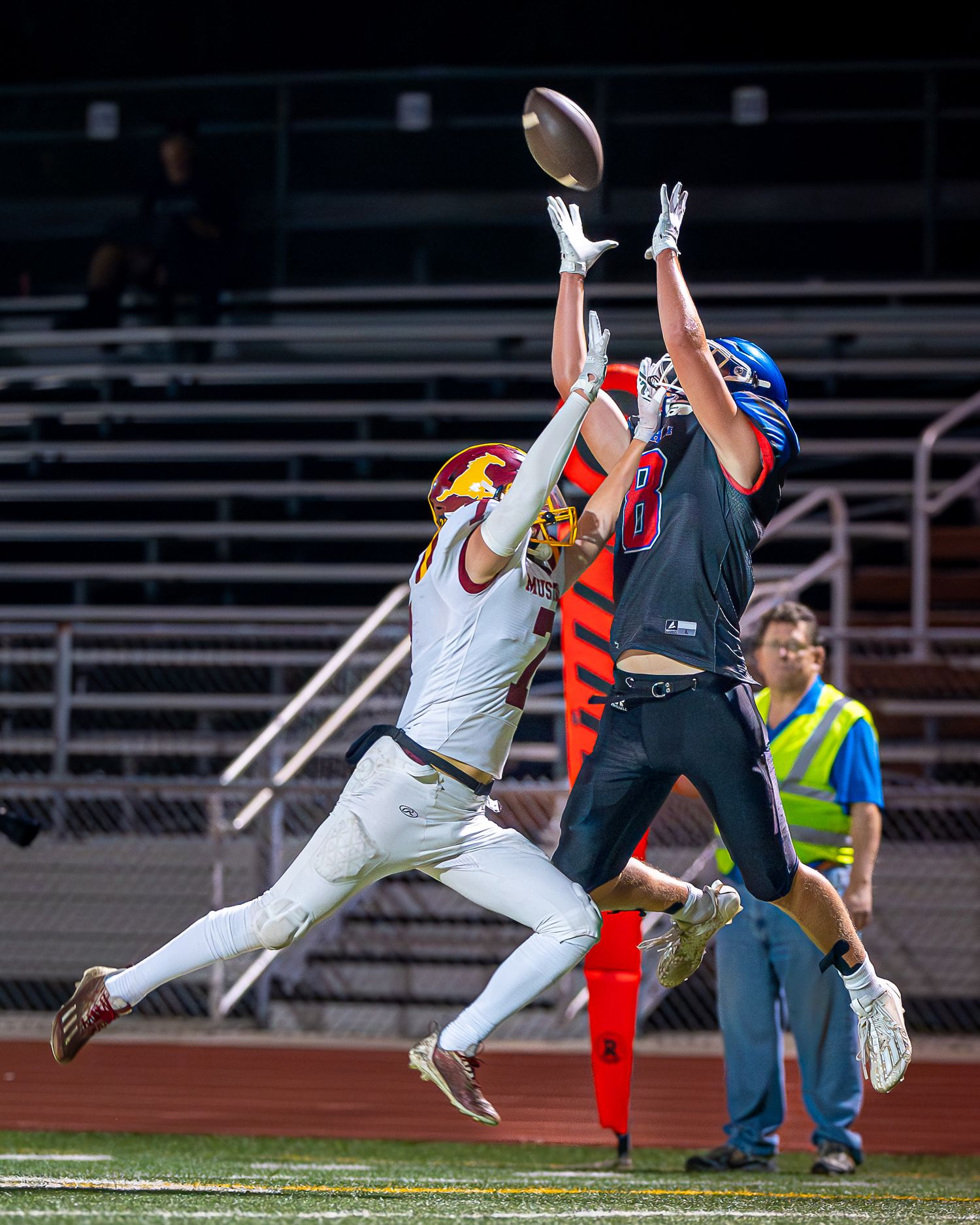Two flag football players leap high to catch ball during competitive night game.
