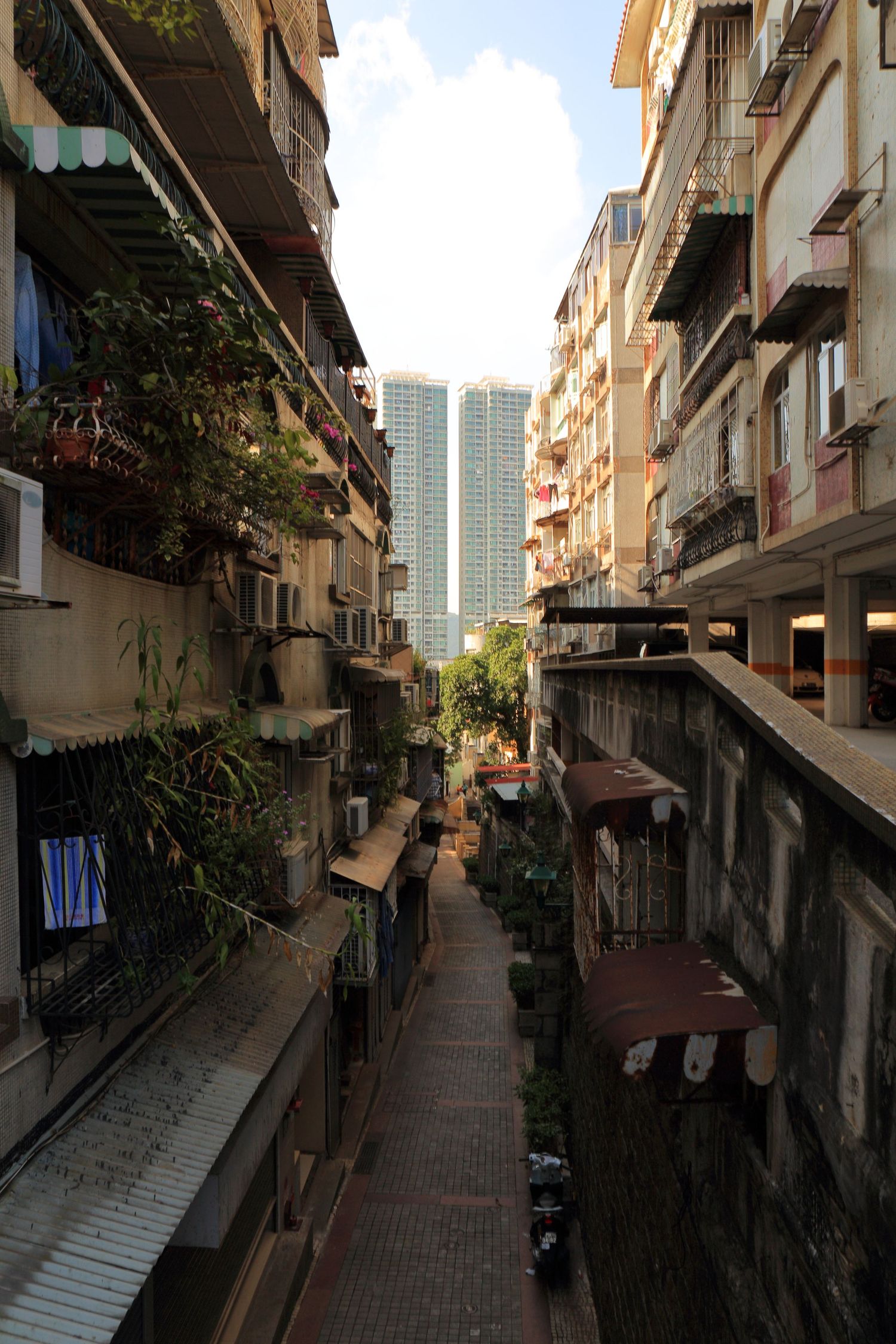 Narrow alley between apartment buildings with modern skyscrapers visible at the end.