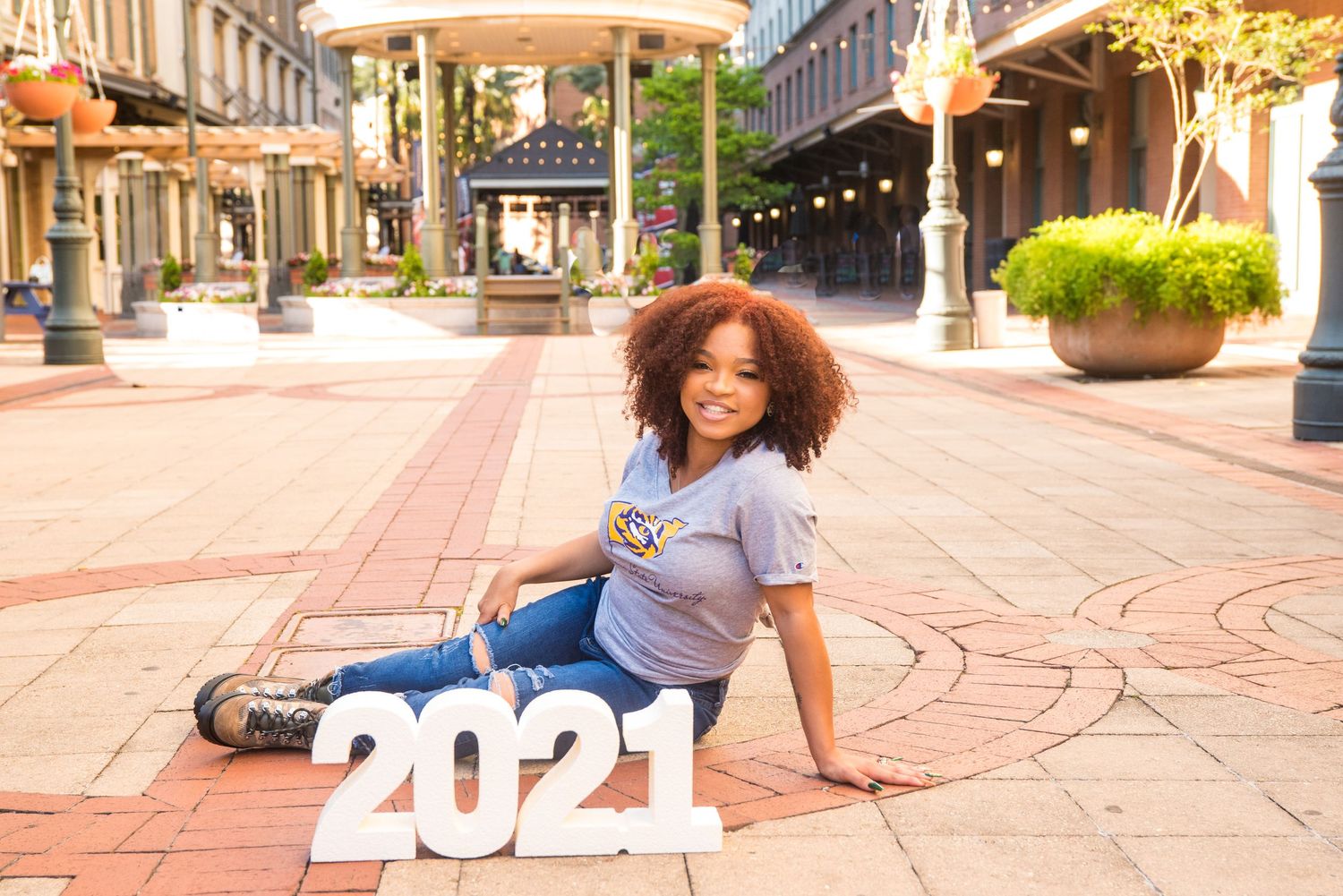 Graduate sitting on brick pavement with decorative 2021 numbers outdoors.