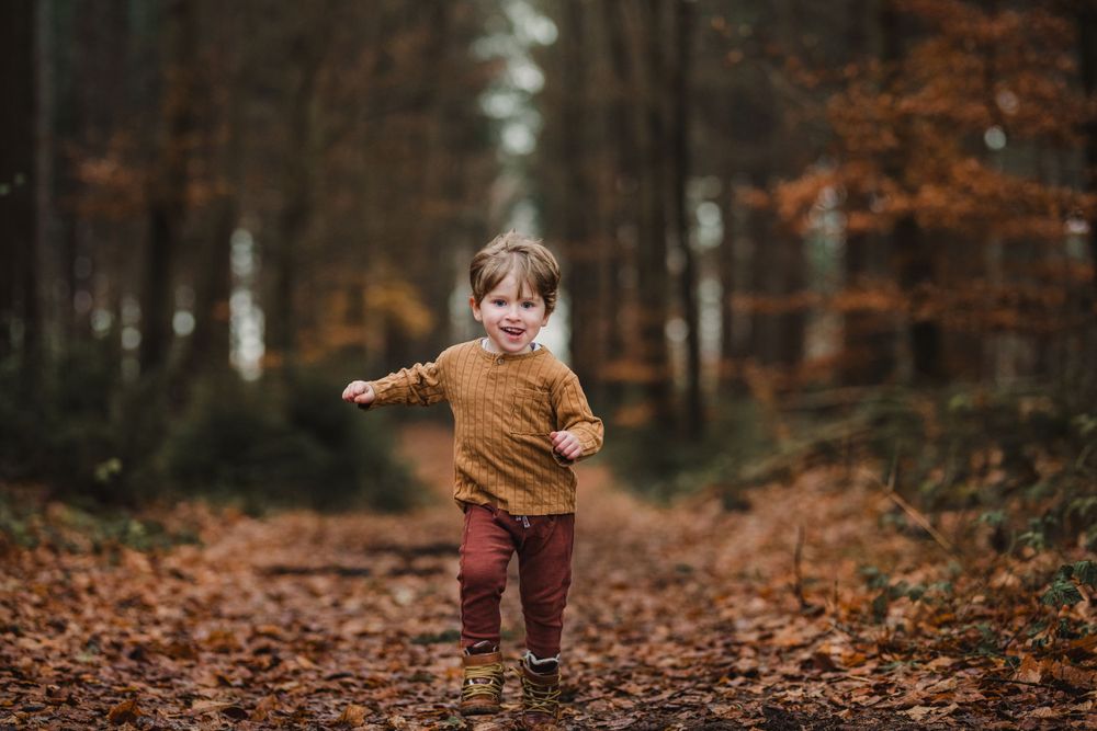 jongen rent in bos vol herfstkleuren tijdens fotoshoot