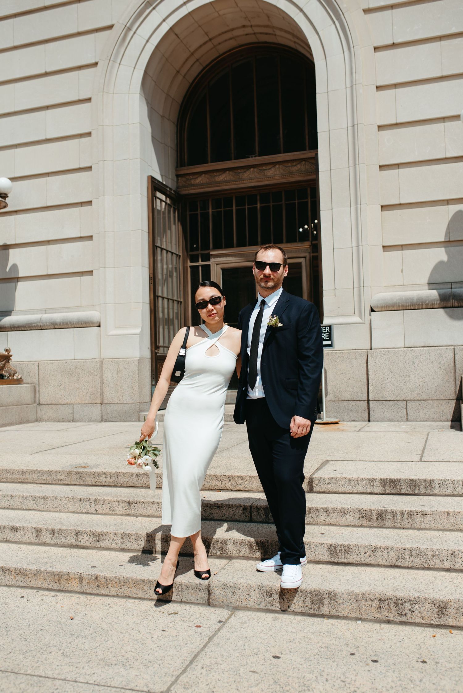 Elegantly dressed couple poses on stone steps of historic building.