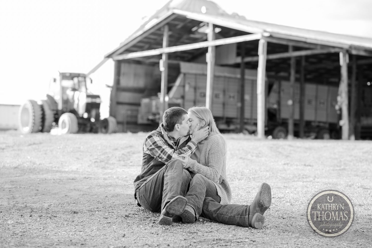 Black and white photo of a couple sitting close together by a barn.