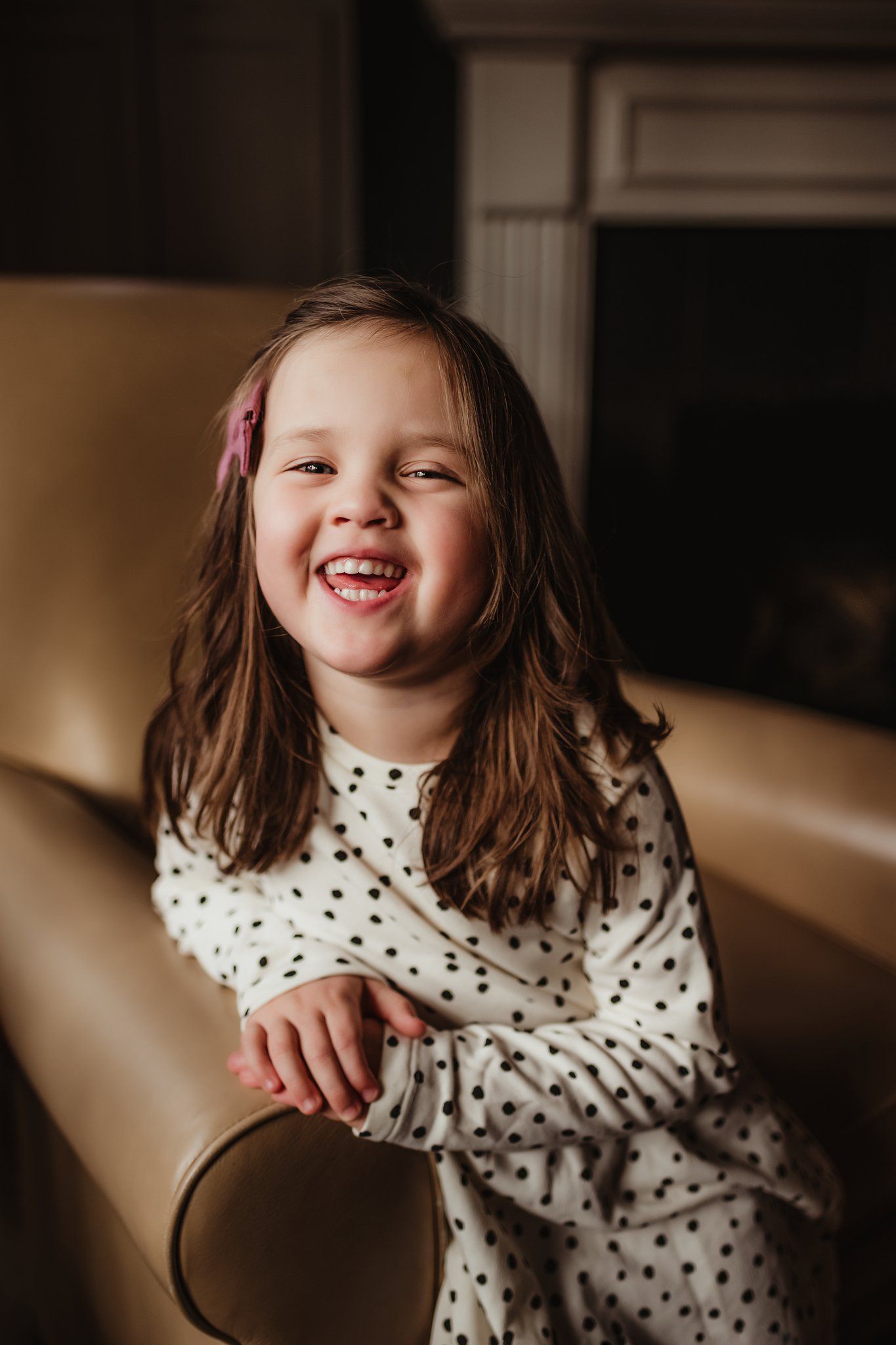 A joyful expression captured on a polka dot dress against a tan leather chair.