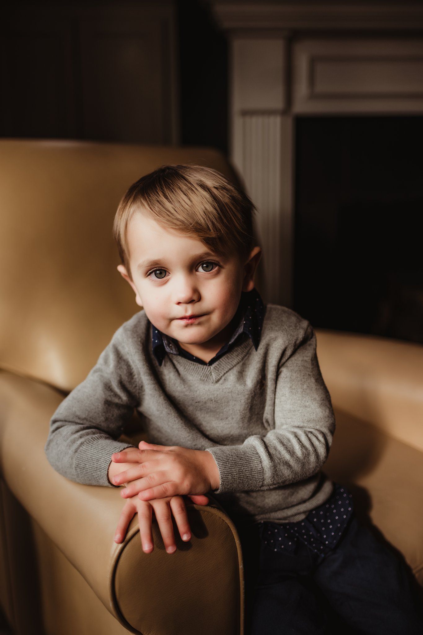 A pensive portrait on a leather chair with warm lighting and classic styling.