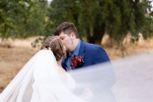 Bride and groom kissing in field with trees. The veil is in the image. Chico, California Wedding