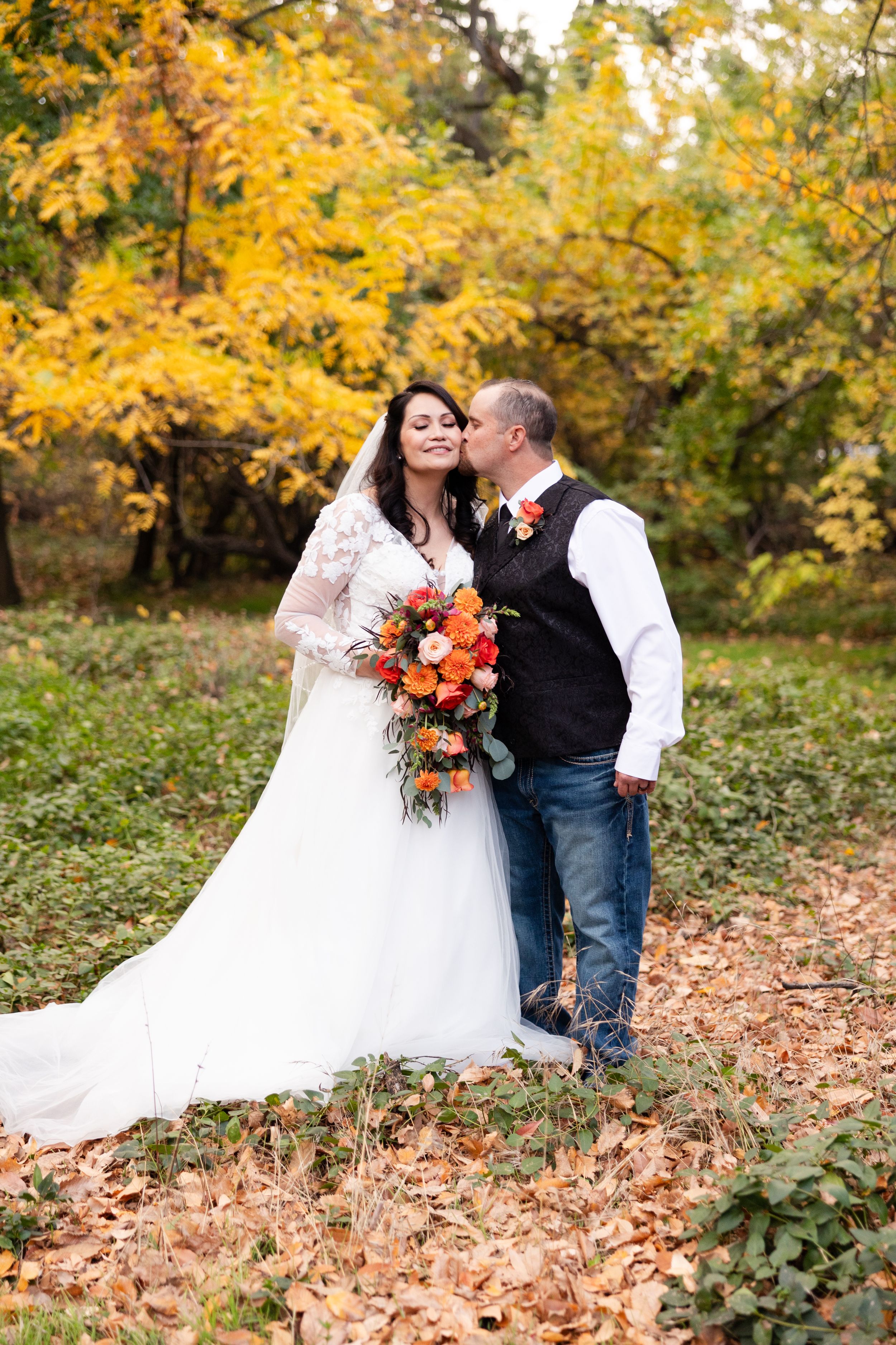 Groom kissing bride at fall wedding with beautiful foliage behind them at Chico Rose Garden, California