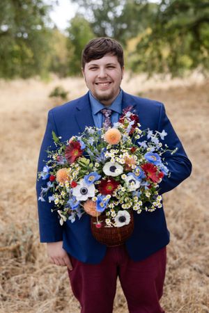 Groom holding the bride's bouquet in field with trees behind him in Chico, California Wedding