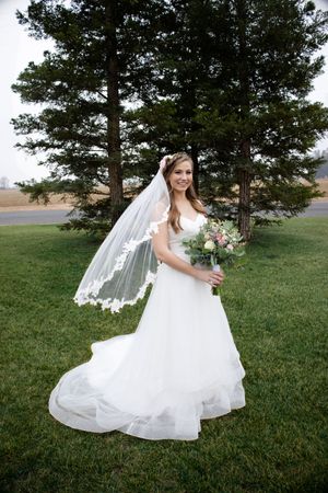 Bridal portraits on beautiful lawn with pine trees behind her with veil blowing at at Orland, California Wedding