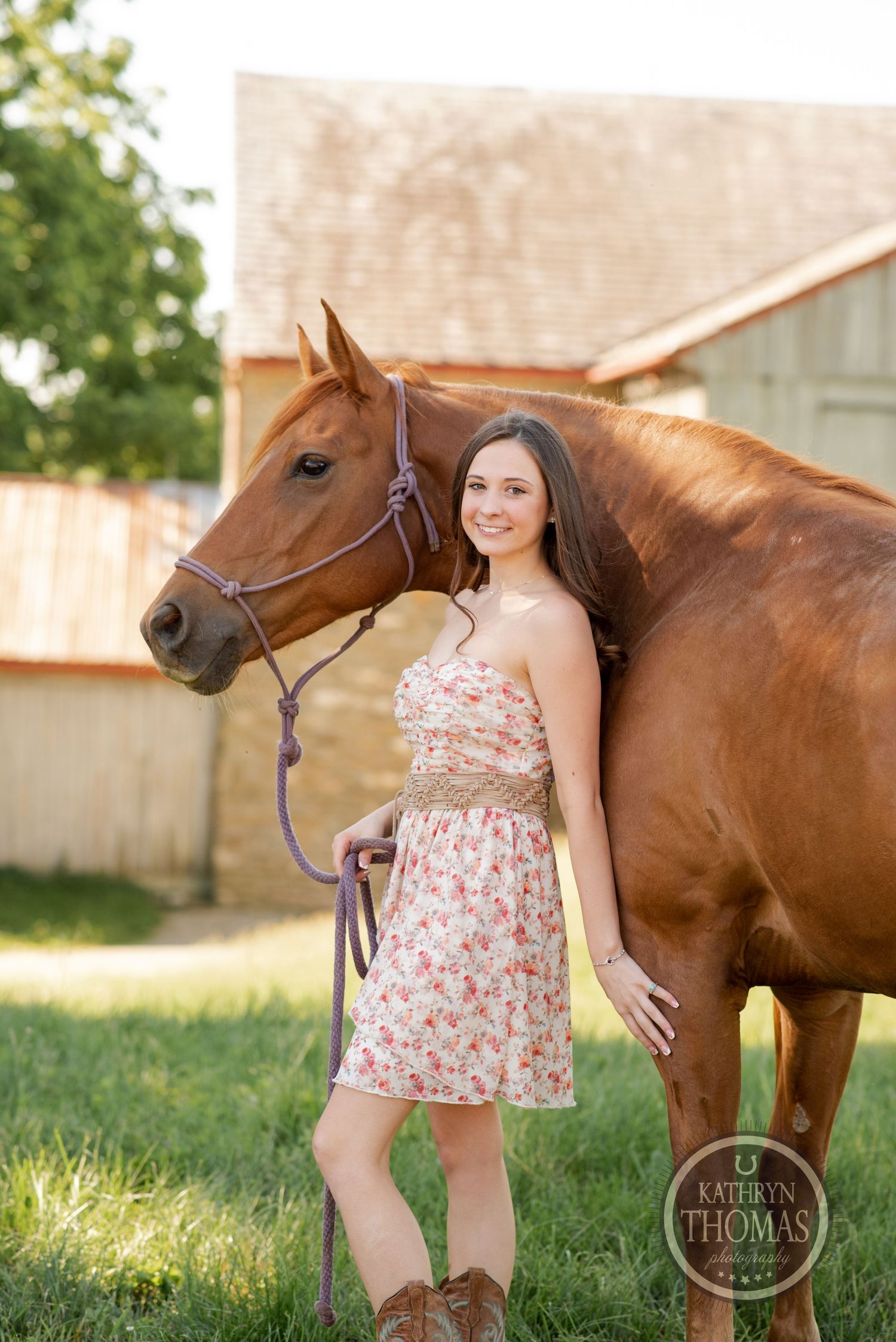 A gorgeous chestnut horse stands beside its rider near a rustic barn backdrop.