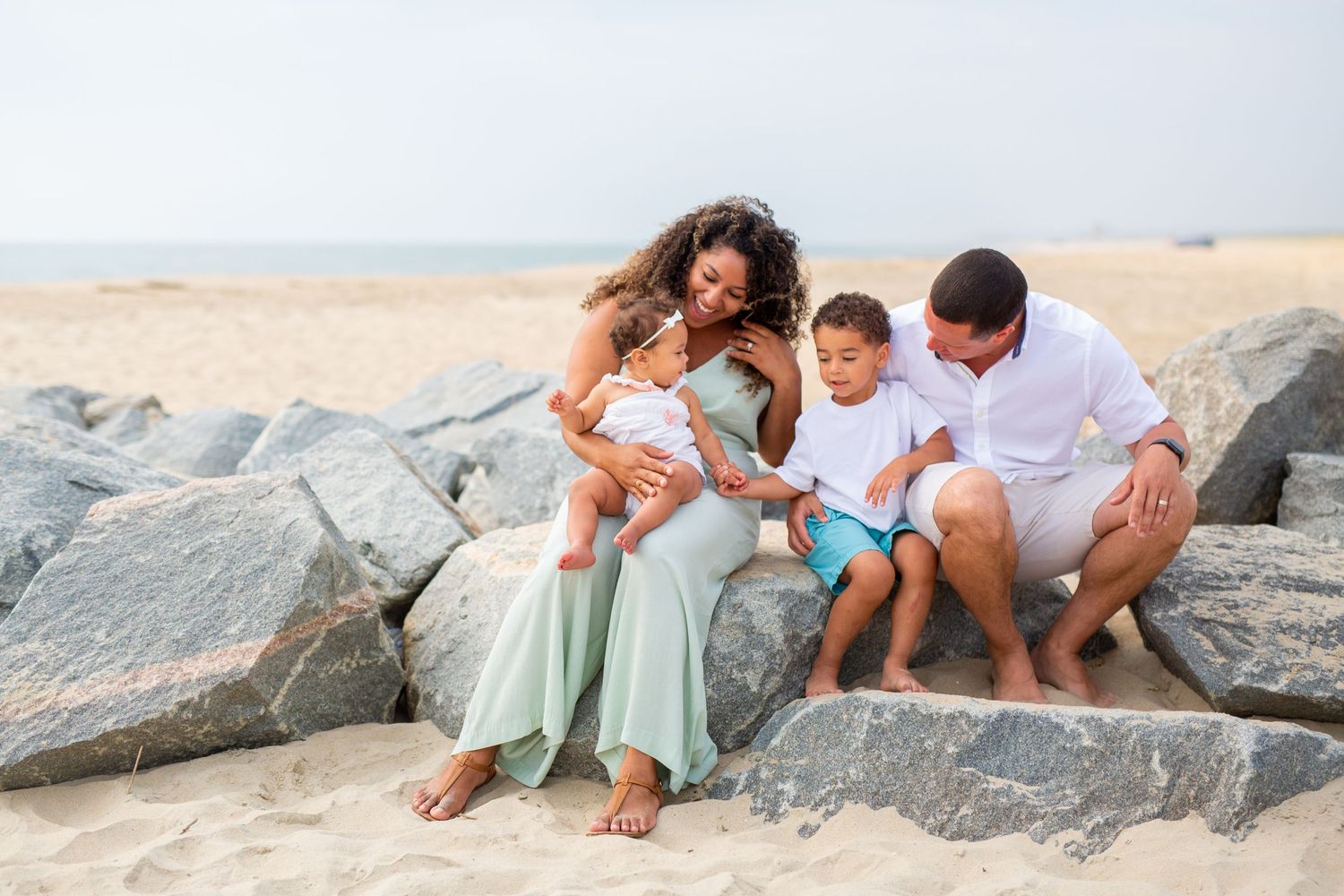 A family shares a tender moment together while sitting on rocky beach outcropping by the ocean.