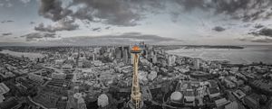 Aerial panoramic cityscape view of a modern city with tall buildings and coast under dramatic clouds.