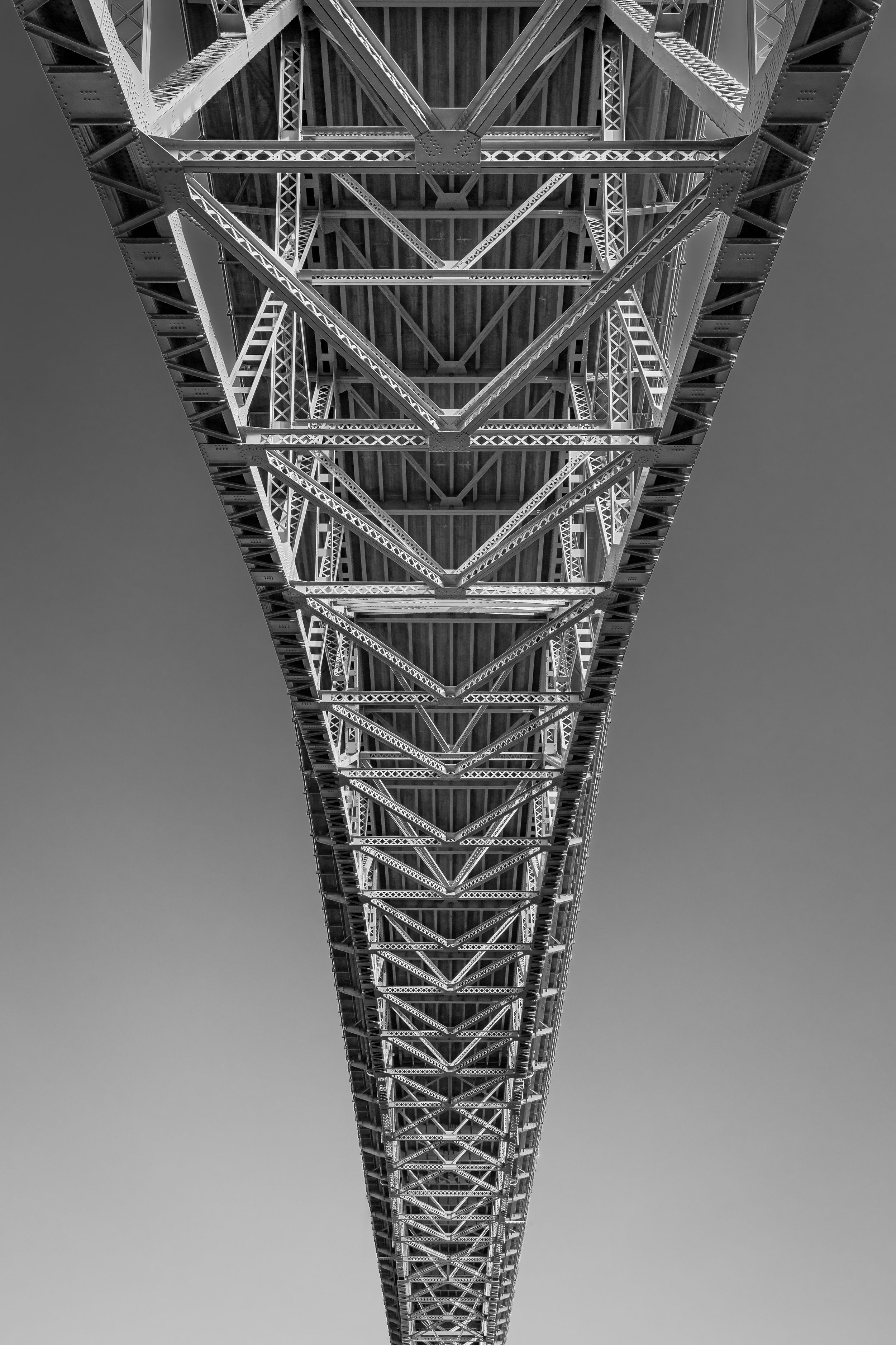 Symmetrical black and white view looking up at geometric steel bridge architecture.