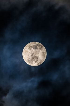 Full moon glowing brightly against dark cloudy night sky.