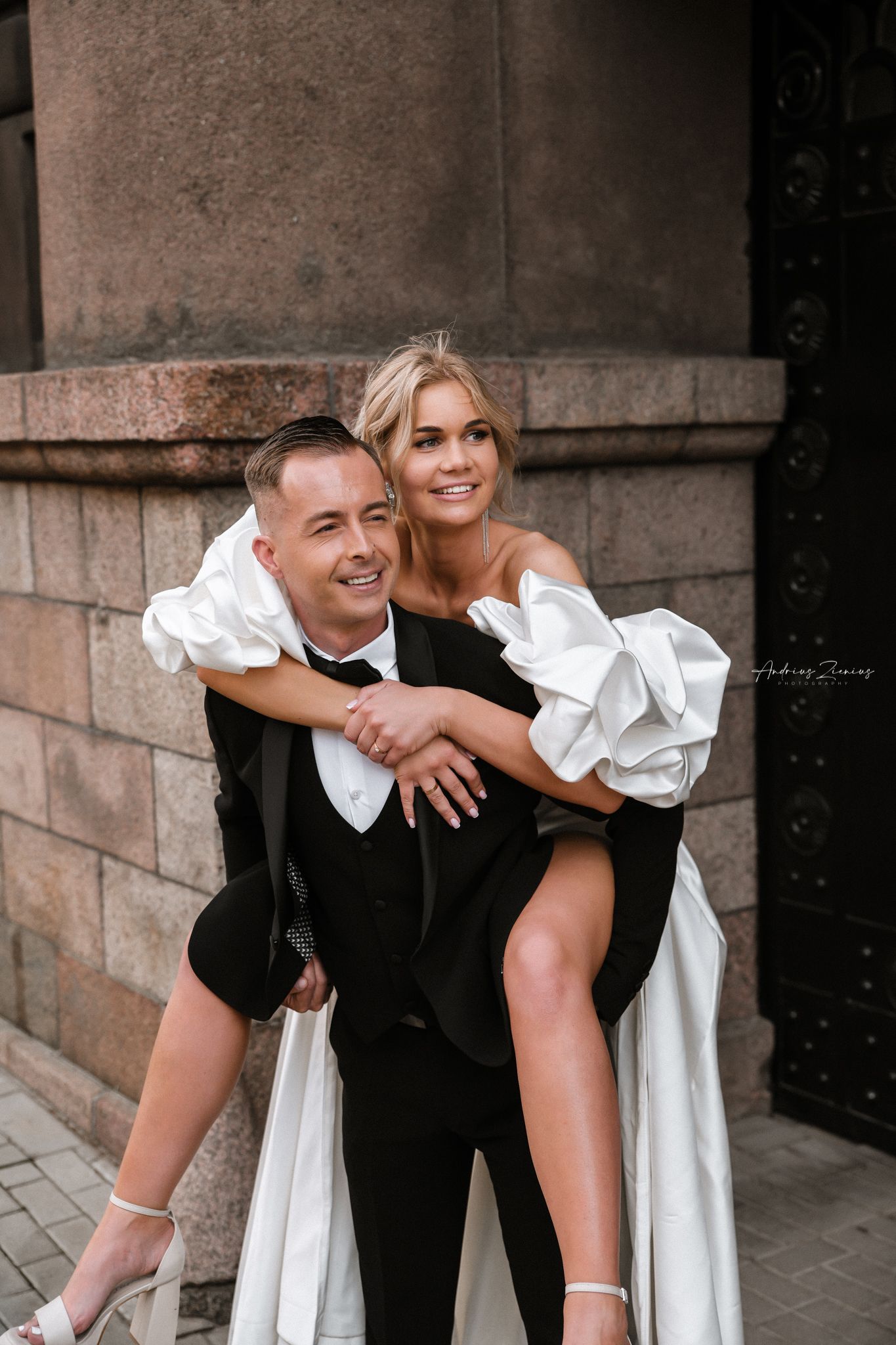 A playful wedding couple poses against a stone wall with the bride getting a piggyback ride.