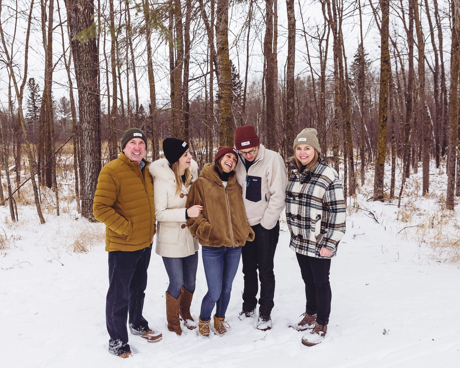 Group of friends in winter coats standing together on snowy path through woods.