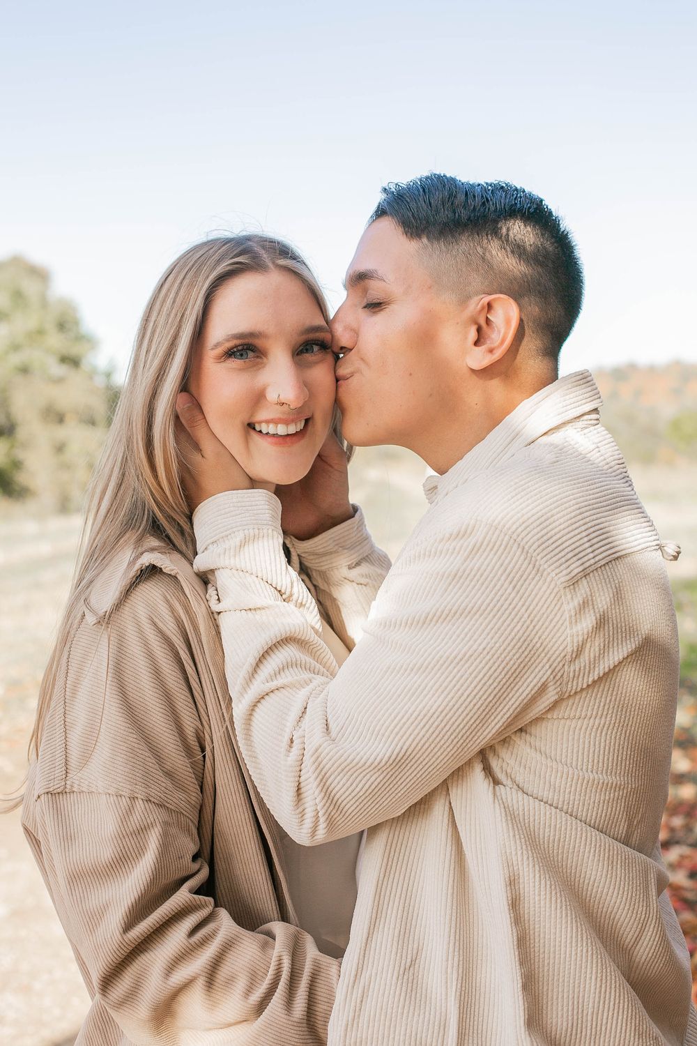 Couple in matching beige outfits sharing tender moment during fall photoshoot.
