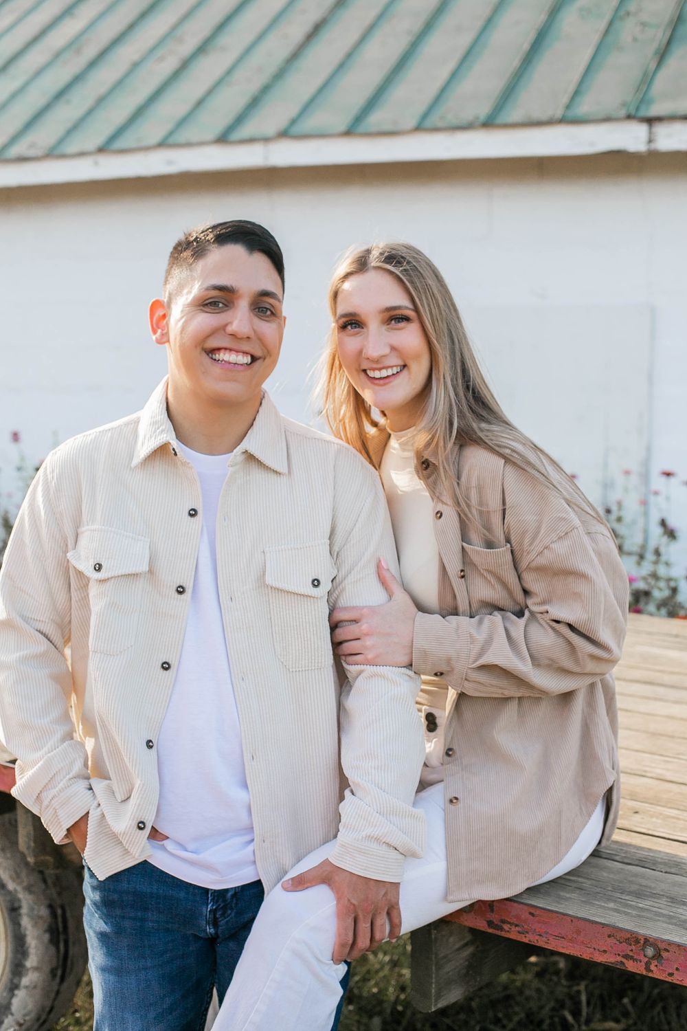 Couple in matching beige jackets smiling together on rustic farm wagon.