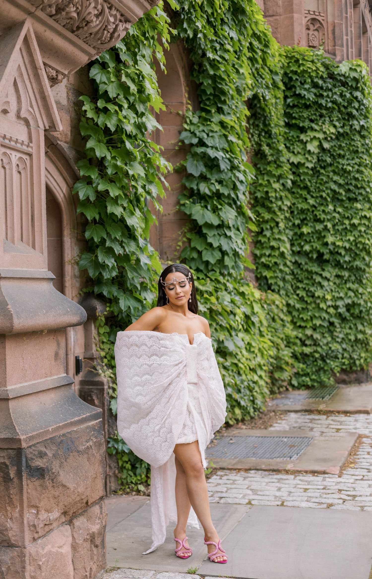 A woman in white poses elegantly against an ivy-covered stone wall.