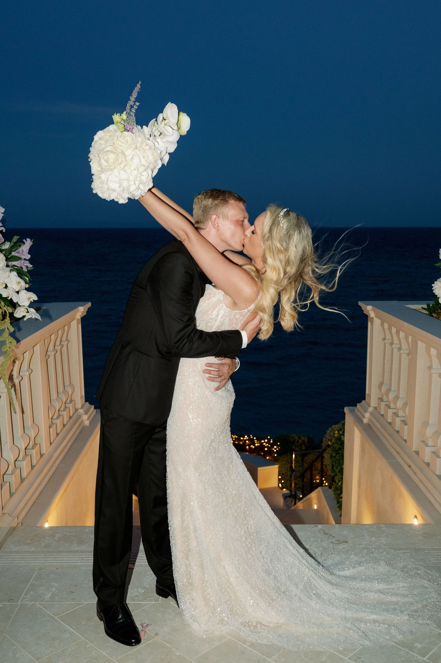 A romantic dip pose during sunset against an ocean backdrop with floral decorations.