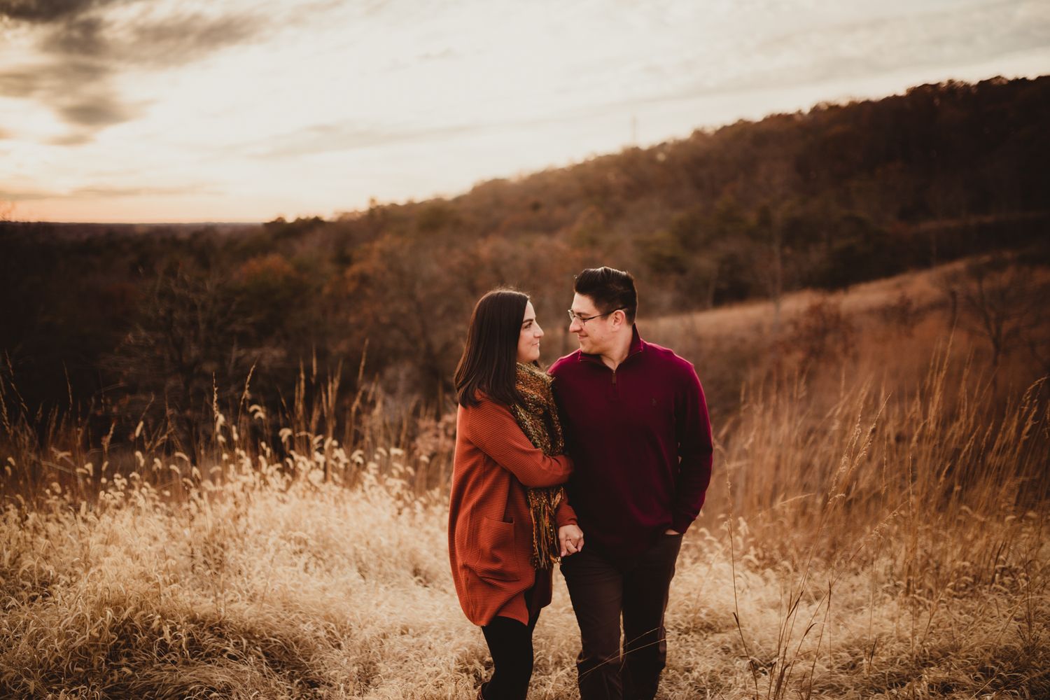 two lovers walk together through a field of tall, brown grass; they hold hands and gaze lovingly at each other