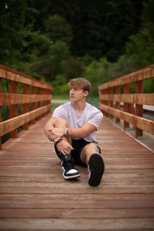Portrait of someone sitting casually on a wooden bridge walkway surrounded by nature.