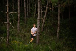 Artistic portrait of someone standing among tall pine trees in a moody forest setting.