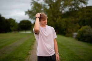 Person in white t-shirt standing in grassy field on overcast day.