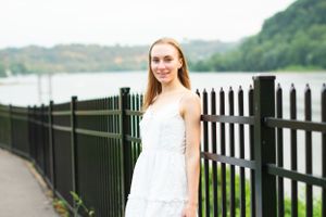 Woman in white dress standing by black metal railing with lake view in background.