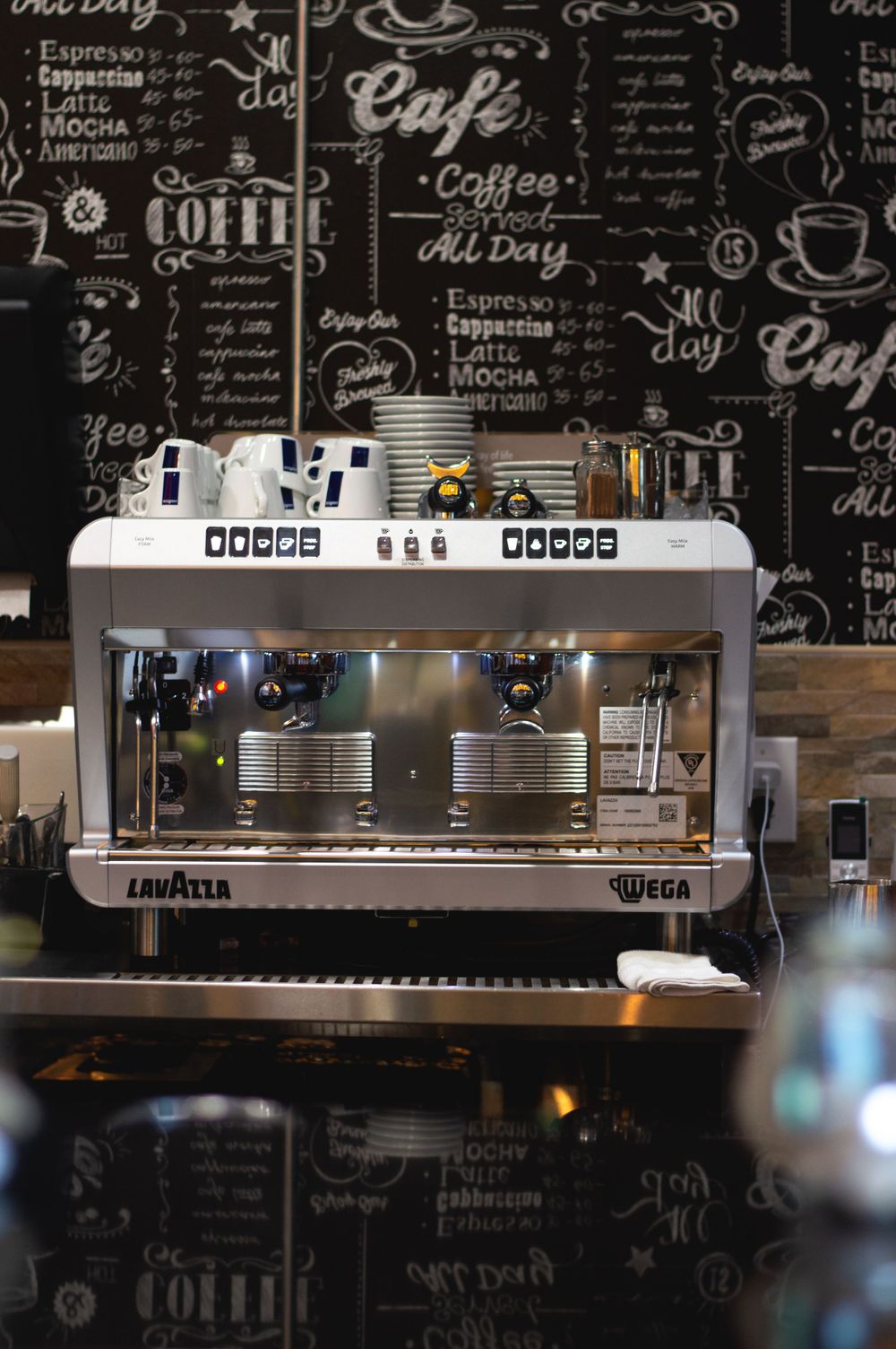 Professional espresso machine with Lavazza branding against a chalkboard wall with coffee-themed typography.