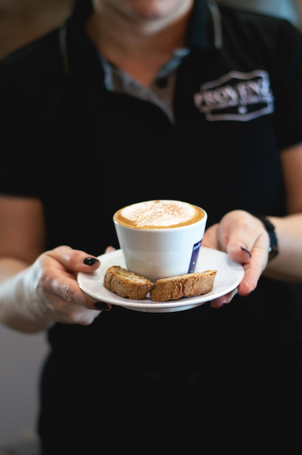 A cappuccino and biscotti being served on a white plate.