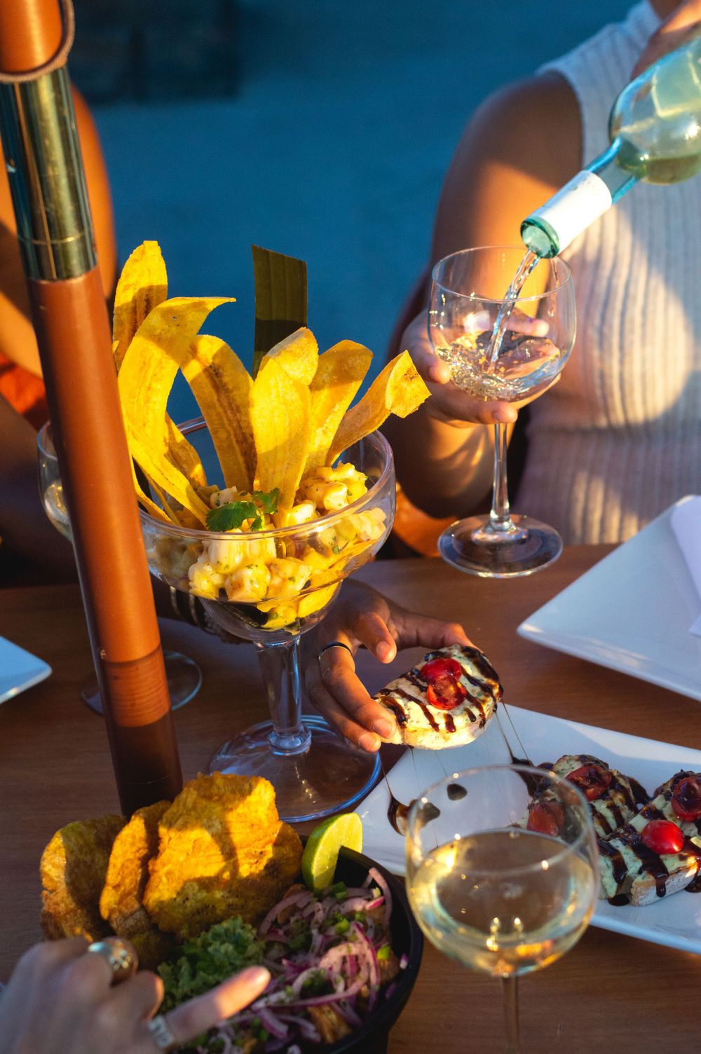 Elegant appetizer platter with yellow flowers and wine service at sunset.