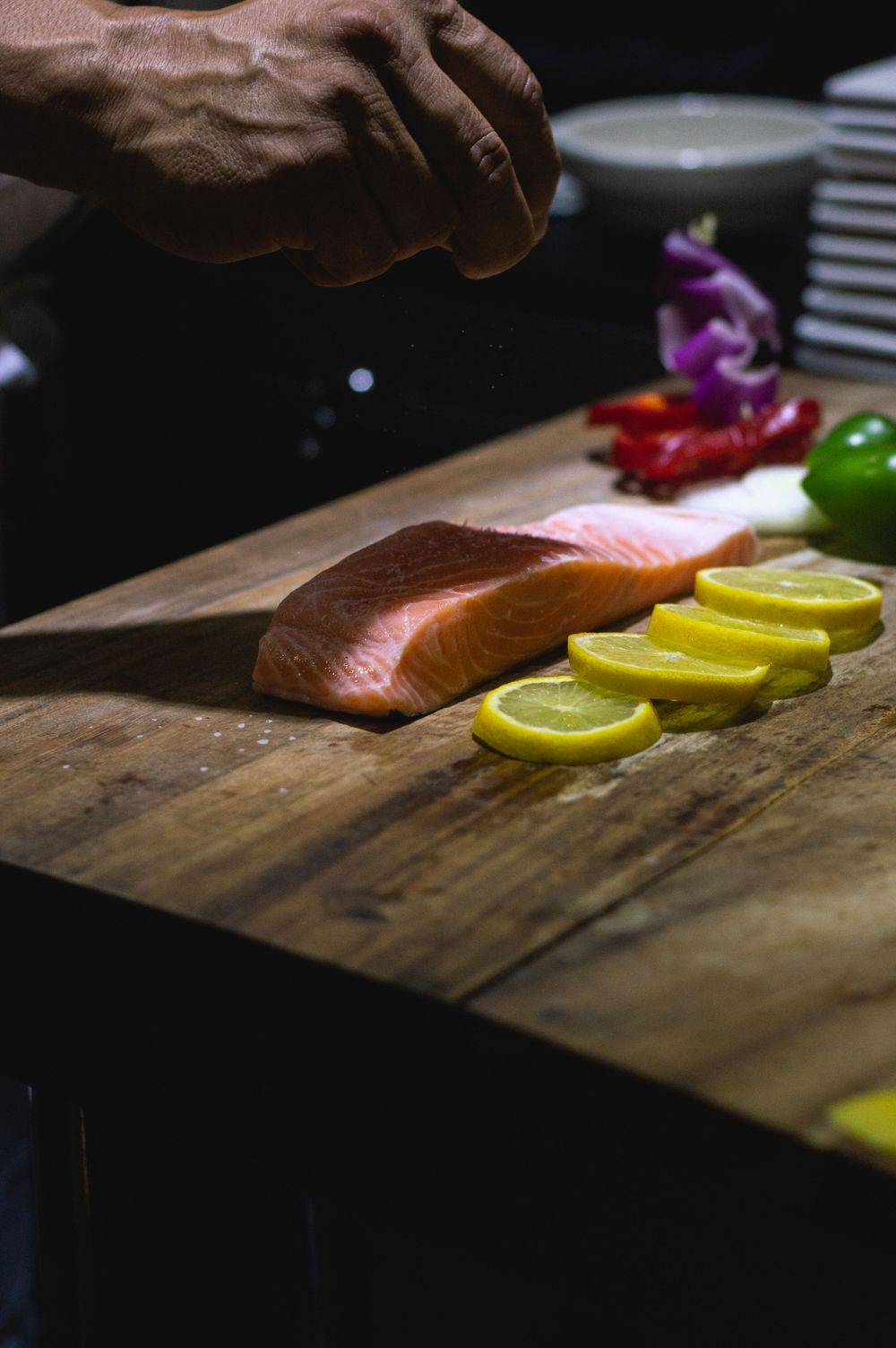 Fresh salmon fillet with sliced citrus on a rustic wooden cutting board in preparation for cooking.