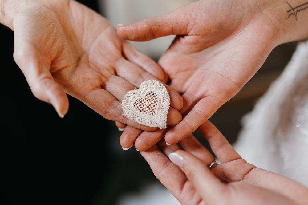 Two people exchanging a small white lace heart keepsake during a wedding ceremony.
