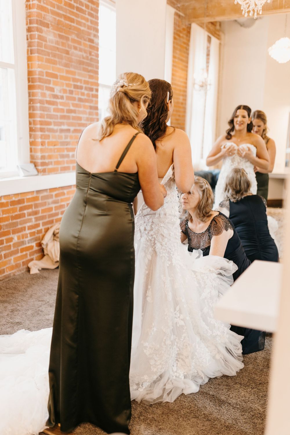 Bridesmaids in black satin dresses helping bride with her elegant lace wedding gown before the ceremony.