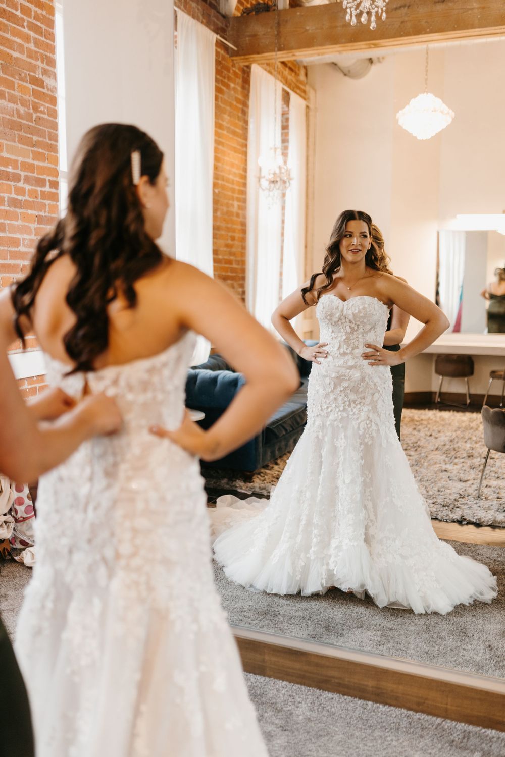 Bride admiring herself in a full-length mirror wearing a stunning strapless floral lace wedding gown.