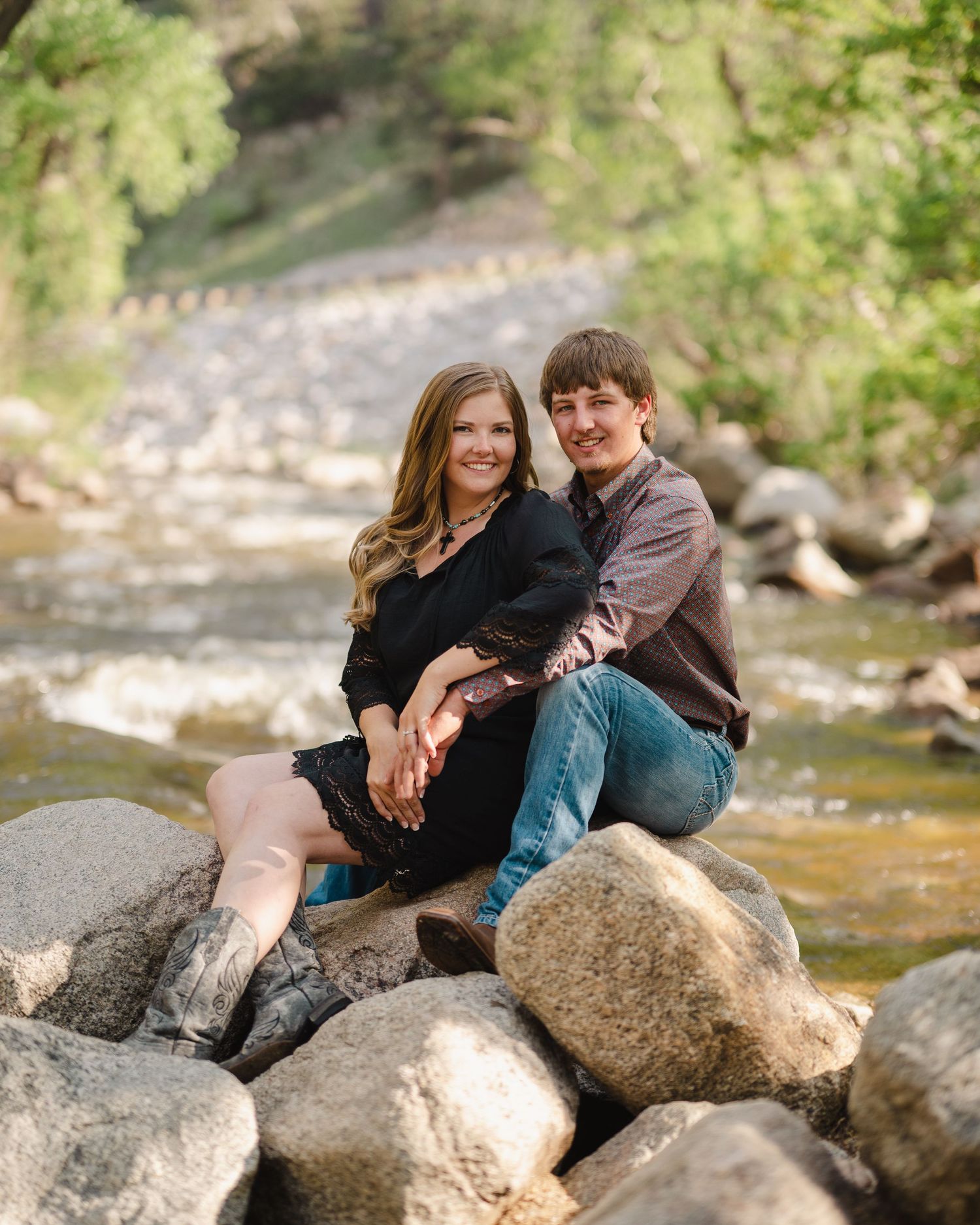 A couple sitting together on rocks by a flowing stream in a scenic outdoor setting.