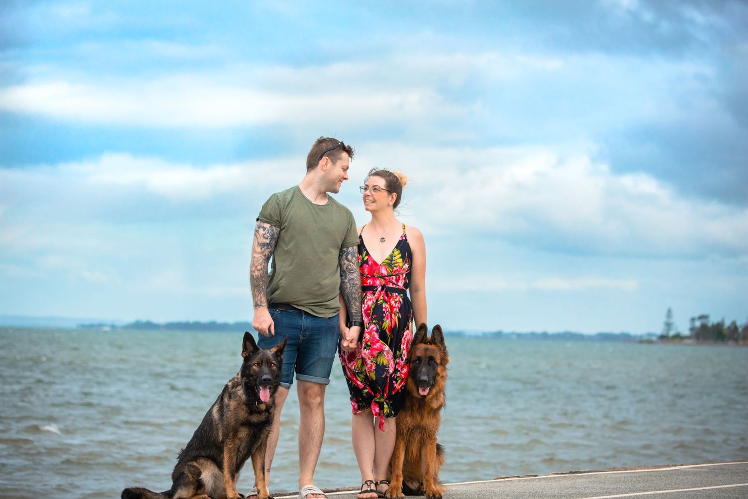 Two people look at each other on the beach while their two German Shepherds sit next to them and look at the camera