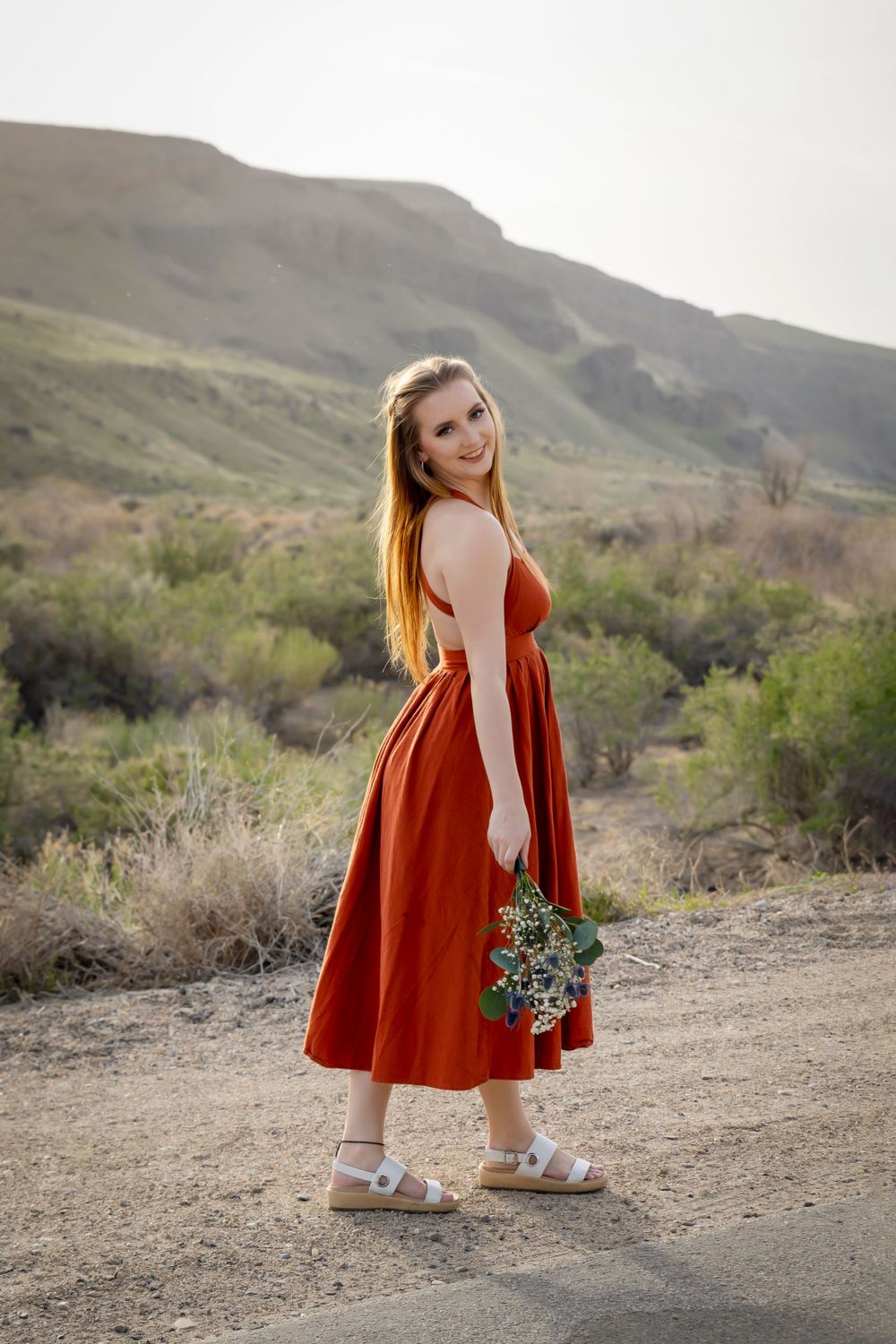 girl wearing orange dress holding wildflowers at sunset