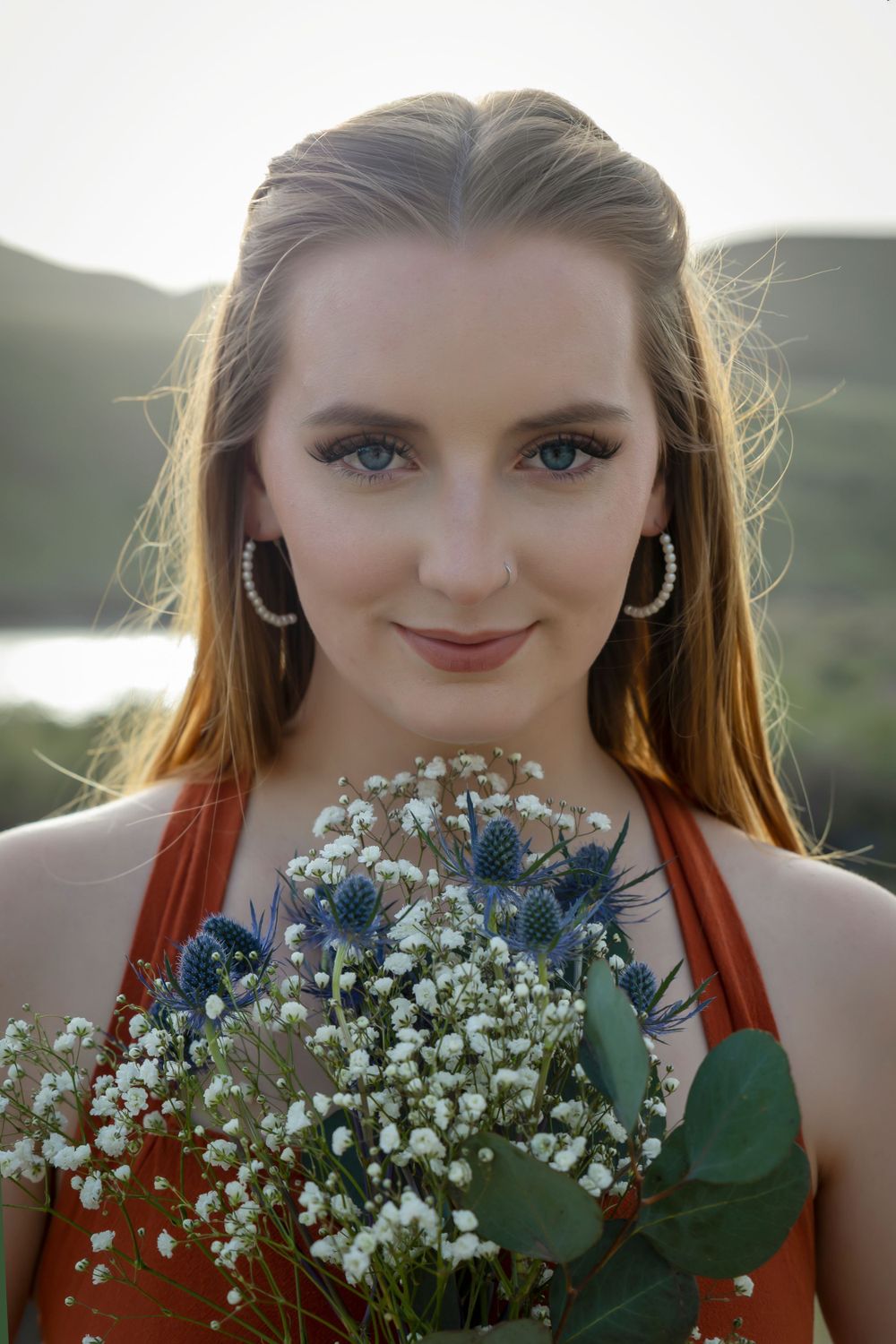 girl wearing orange dress holding wildflowers at sunset