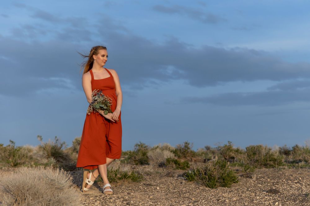 girl wearing orange dress holding wildflowers at sunset blue skies