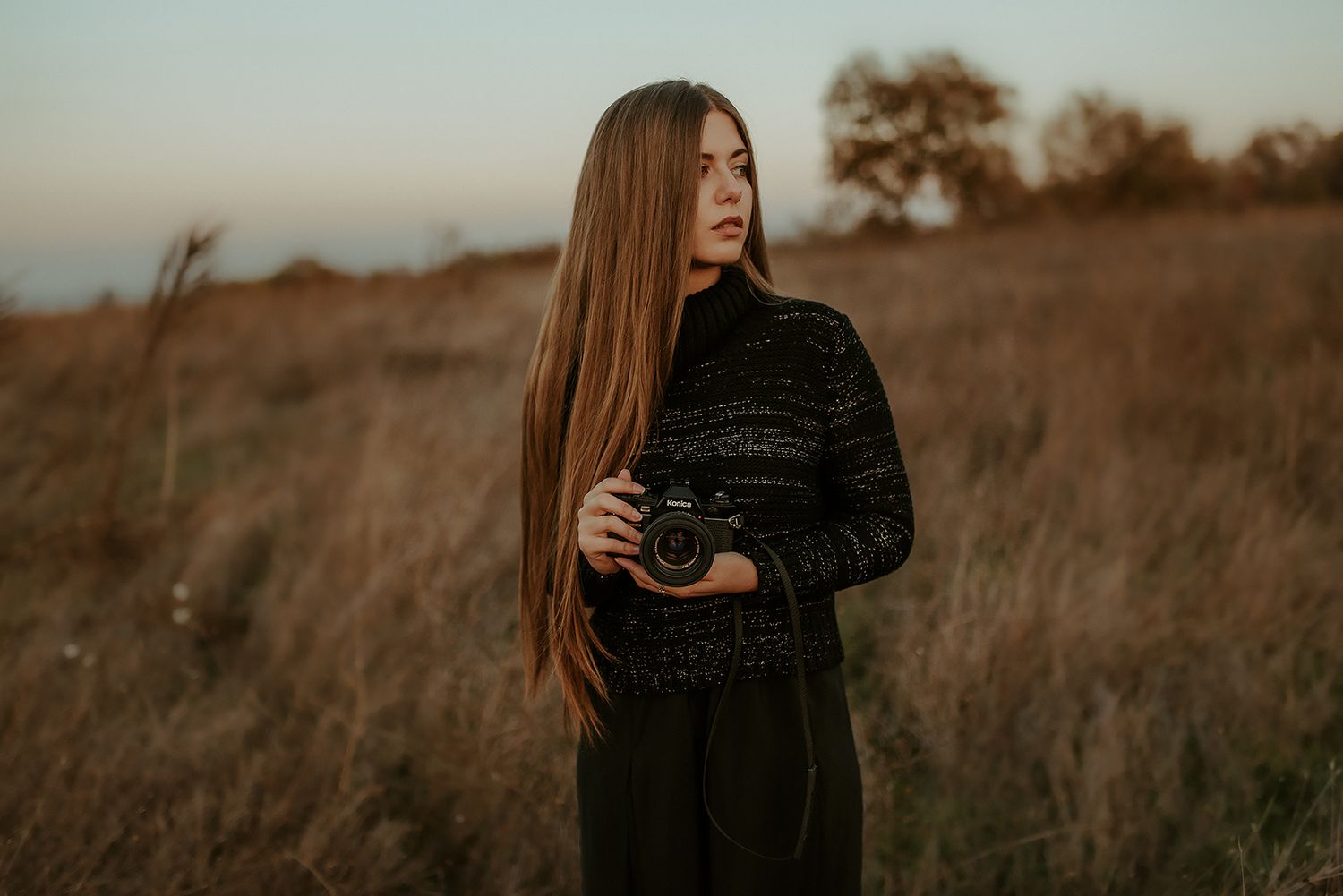 Photographer in black holding camera in golden field at sunset.