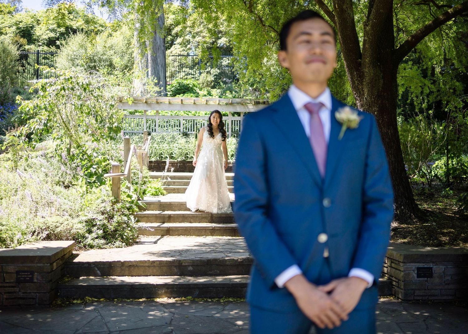 Wedding photo in lush garden with stone steps and weeping willow trees.