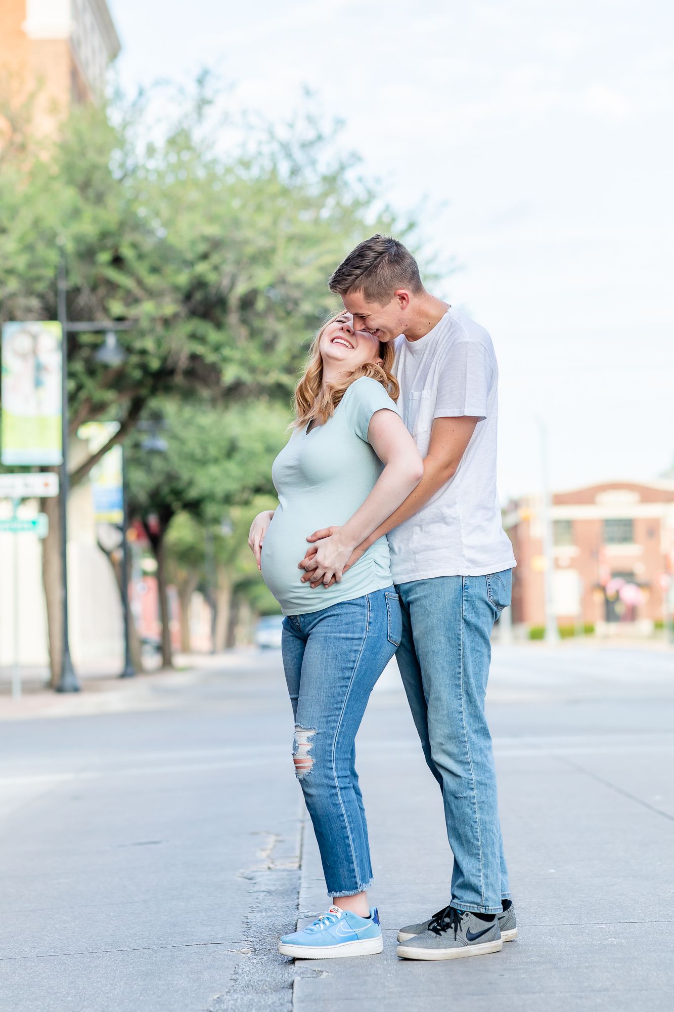 Couple expecting their first baby snuggle and laugh in the street in Abilene, Texas.