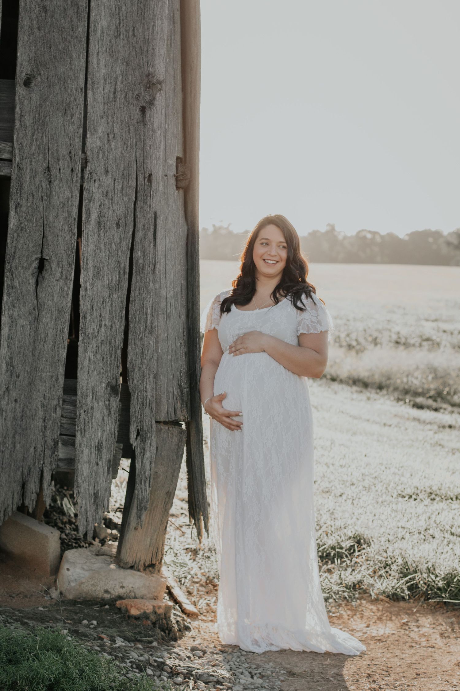 Woman in white dress standing between trees in sunlit field.